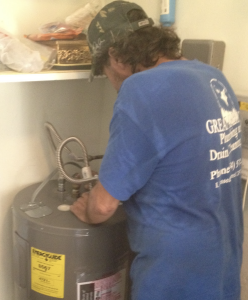 Plumber in blue shirt working on a water heater, showcasing Great American Plumbing's repair services in Cooper City.